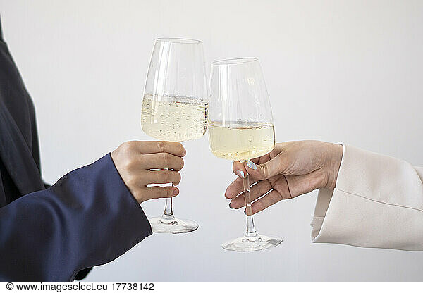 Hands of women toasting wineglasses in front of white wall