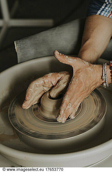 Hands of young man molding clay on potter's wheel in workshop