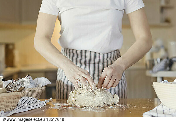 Hands of young woman kneading dough on table