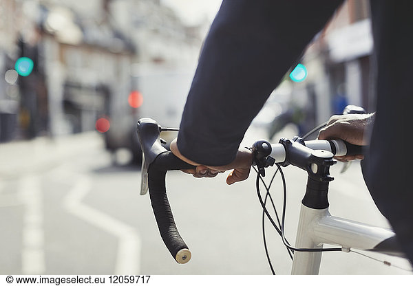 Hands on man on bicycle handlebars  commuting on sunny urban street