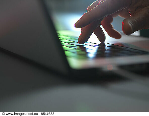 Hands touching laptop keyboard in dark at home office