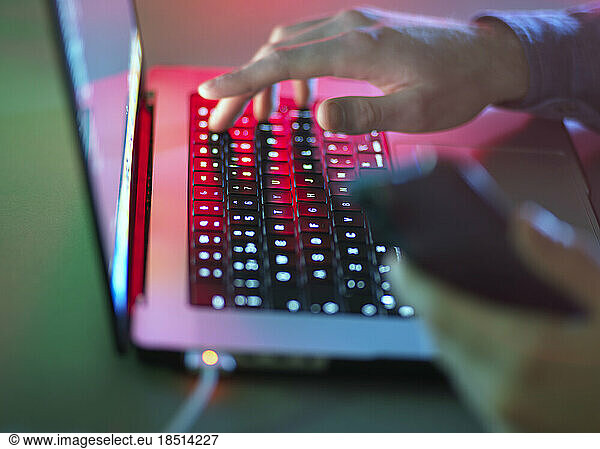 Hands typing on laptop keyboard in dark at office