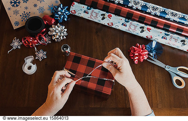 Hands wrapping present at wooden table with gift wrapping supplies.