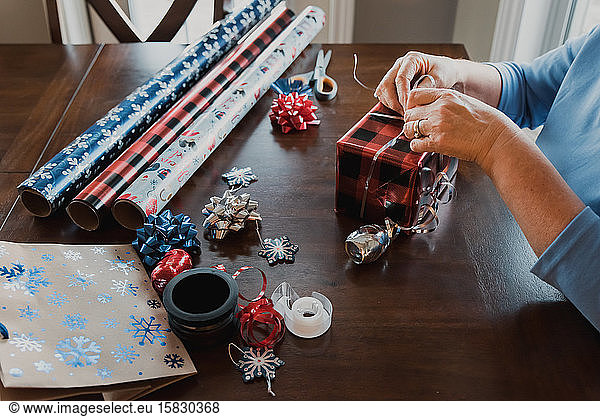 Hands wrapping present with gift wrapping supplies on table.