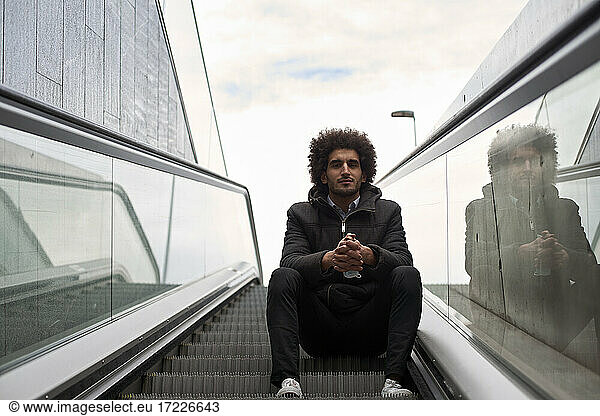 Handsome Afro man sitting on escalator by sky