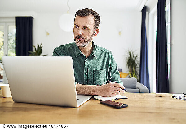 Handsome man working from home taking notes at desk