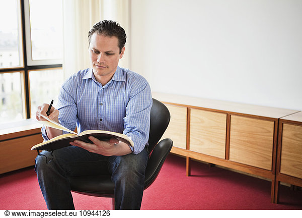 Handsome mid adult man sitting while writing in book