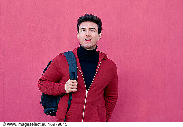 Handsome student man poses with a backpack on a pink background