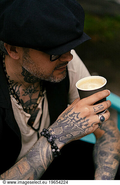 Handsome stylish man drinks coffee  his hands are covered in tattoos.