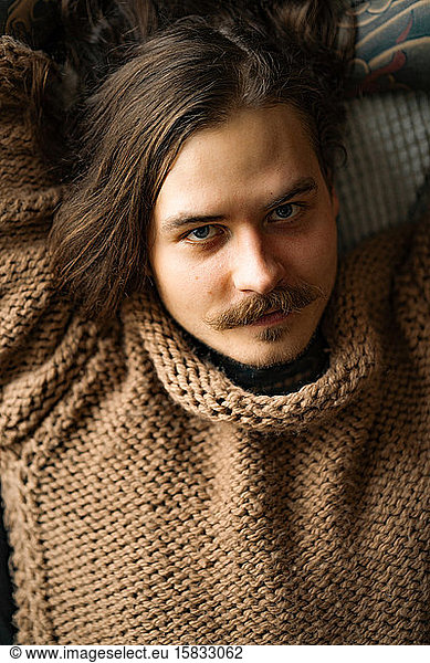 Handsome tattooed sexy man with long hair and mustache at sofa