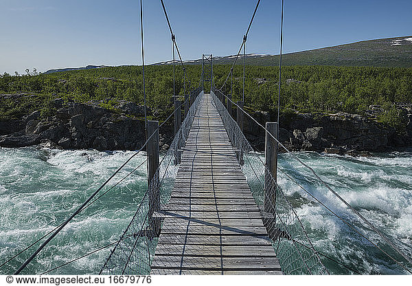 Hanging bridge over flowing water of Vuojatädno river along Padjelantaleden Trail  Lapland  Sweden