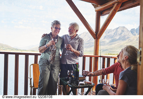 Happy active senior couples drinking wine on summer balcony