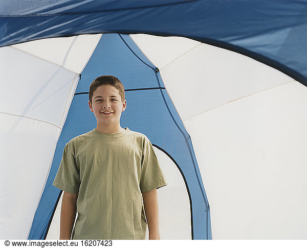 Happy adolescent boy standing upright in a dome camping tent