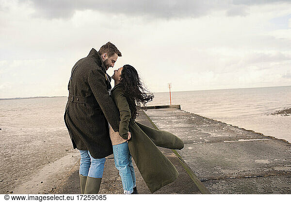 Happy affectionate couple in winter coats on ocean beach