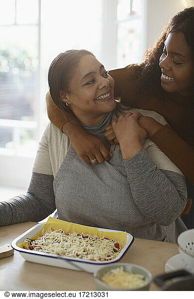 Happy affectionate mother and daughter making homemade lasagna
