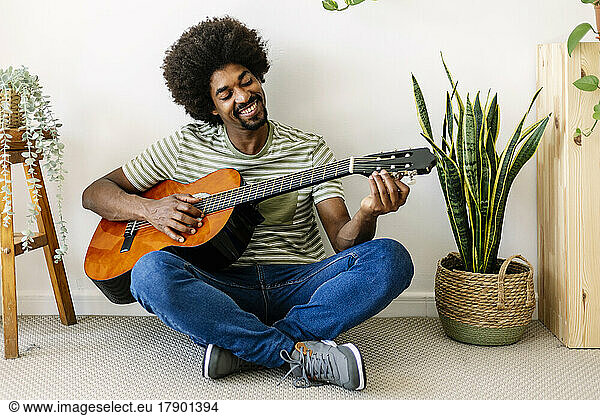 Happy African man playing guitar in front of wall at home