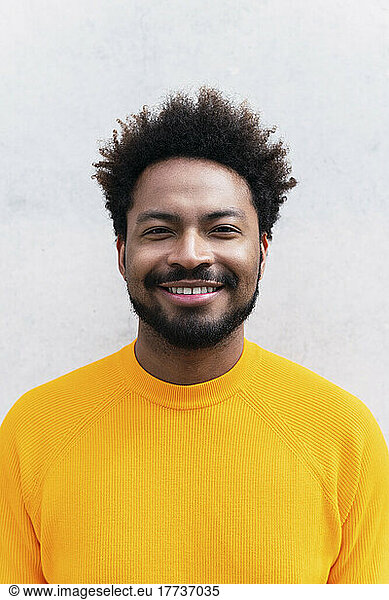 Happy Afro man wearing yellow t-shirt in front of white wall