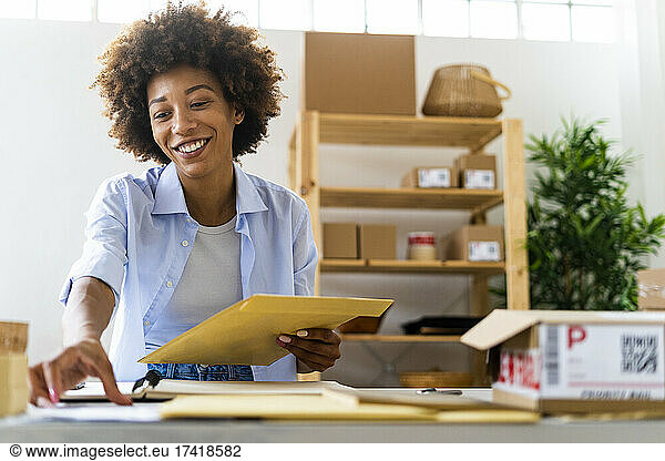 Happy Afro woman holding parcel while siting at desk in studio