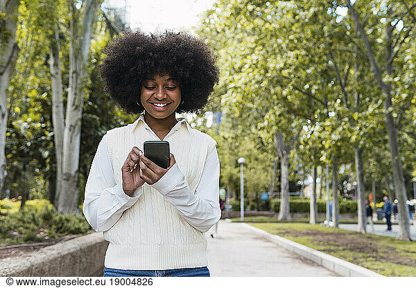 Happy Afro woman using smart phone in park