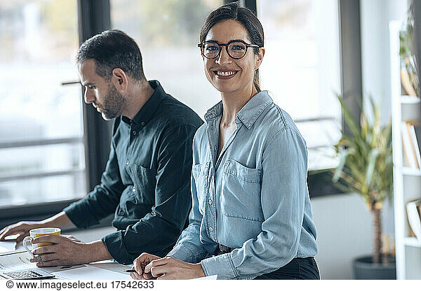 Happy architect wearing eyeglasses sitting by colleague working in office