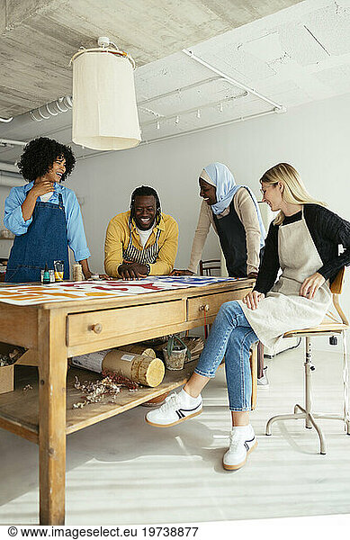 Happy artists discussing with paintings on desk in studio