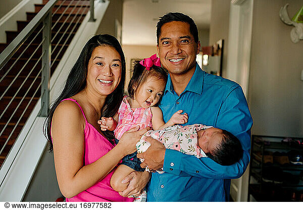 Happy asian parents holding newborn infant and young daughter