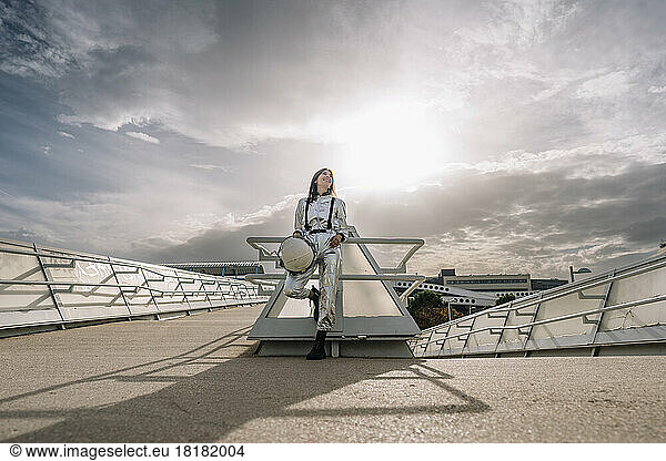 Happy astronaut holding space helmet leaning on railing in front of sky