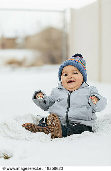 happy baby boy playing in snow outside in snowsuit and beanie