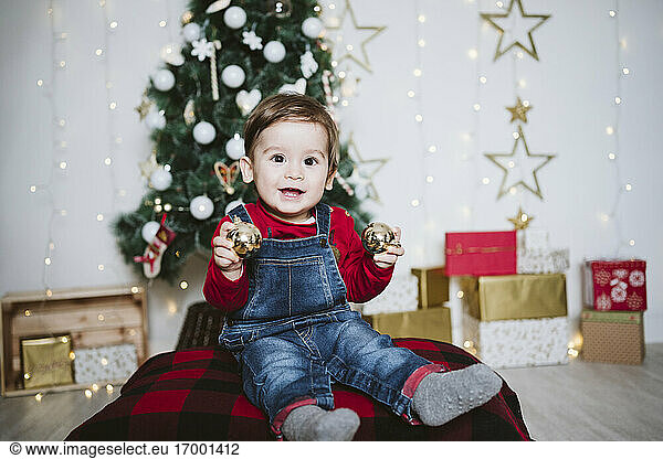 Happy baby boy playing with bauble while sitting at home during Christmas