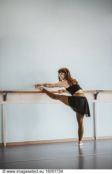 Happy ballet dancer stretching leg in dance studio