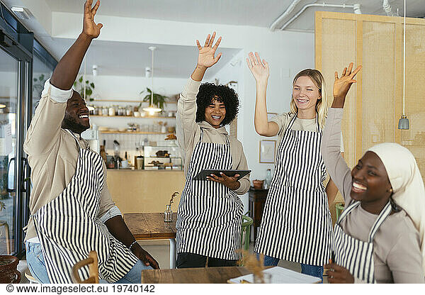 Happy baristas with hands raised celebrating achievement in coffee shop
