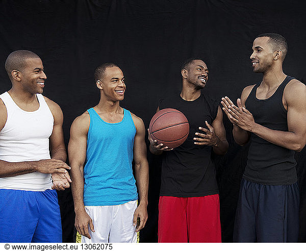 Happy basketball players talking while standing against black wall