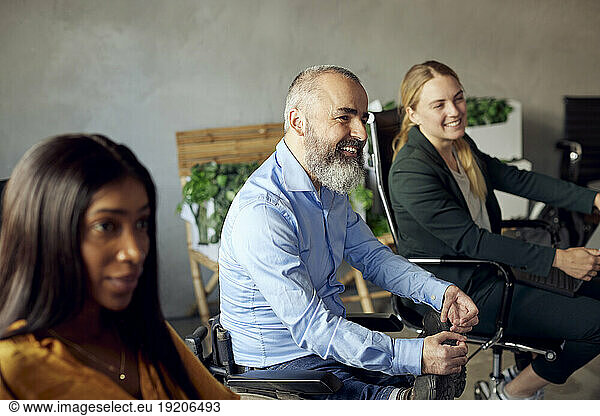 Happy bearded businessman with disability sitting amidst female colleagues in creative office