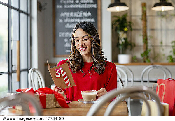 Happy beautiful woman reading Christmas card sitting in cafe