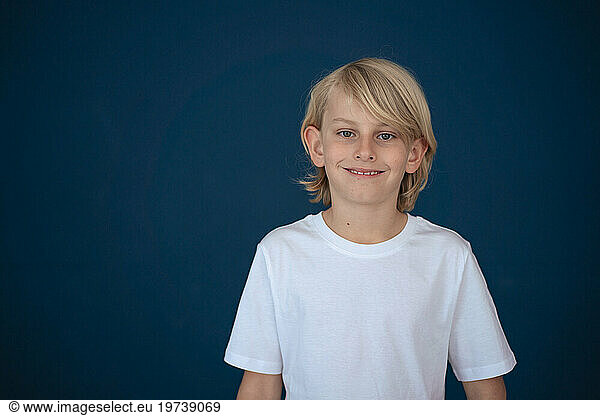 Happy blond boy standing against blue background