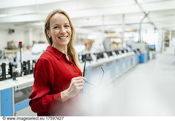 Happy blond businesswoman holding eyeglasses in industry