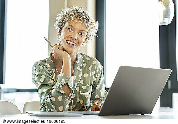 Happy blond businesswoman sitting with laptop at table