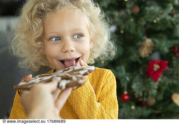 Happy blond girl eating gingerbread at home