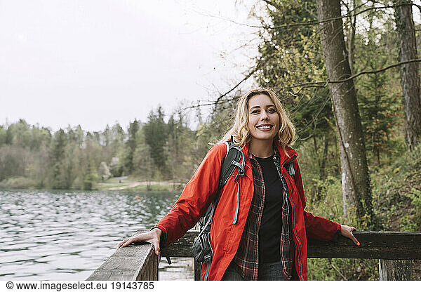 Happy blond hiker standing near railing by lake