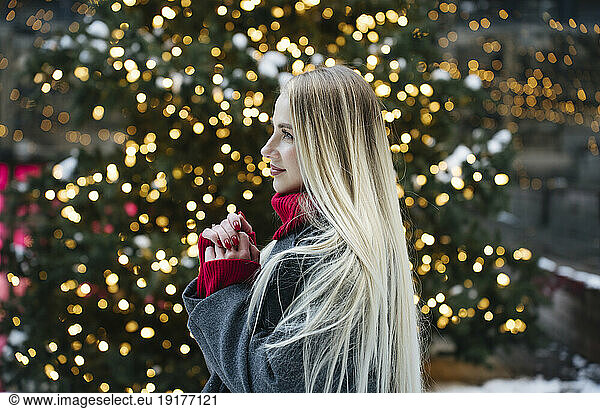 Happy blond woman standing in front of Christmas tree