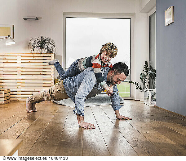 Happy boy balancing on back of father doing push-ups at home