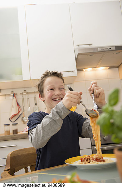 Happy boy eating spaghetti in kitchen