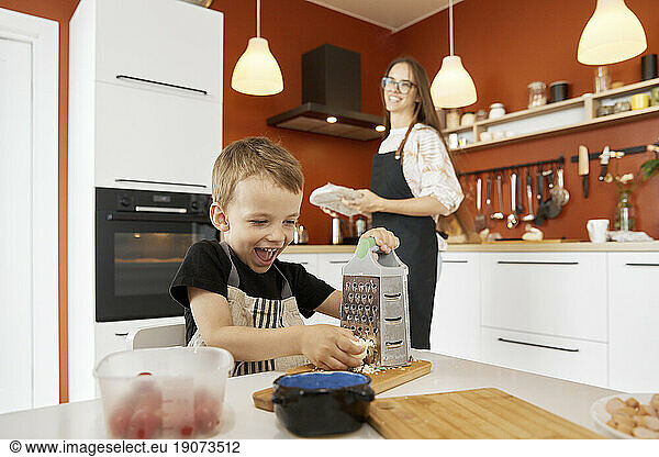Happy boy grating cheese and preparing food with mother at home