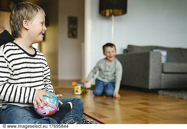 Happy boy having down syndrome with ball sitting on floor in living room