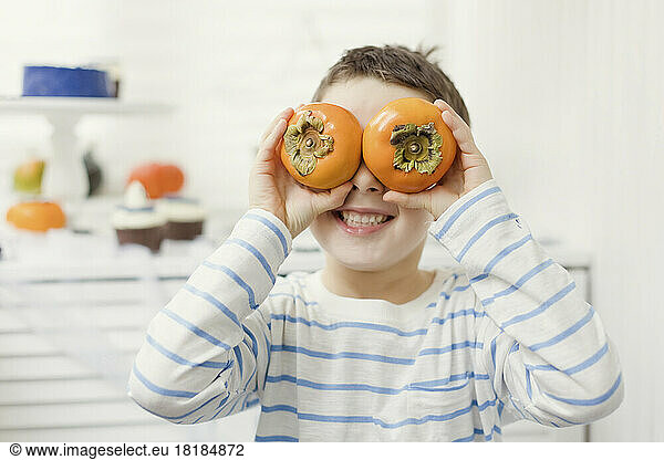 Happy boy holding persimmons over eyes at home