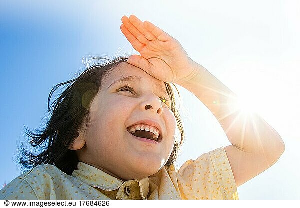 Happy boy in flare sunshine with hand at forehead