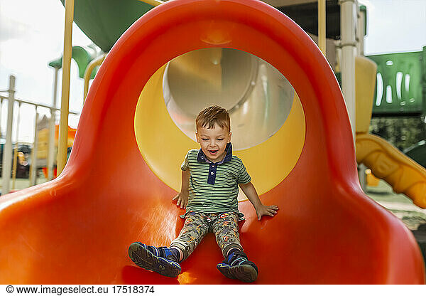 Happy boy in green t-shirt sliding down the slide