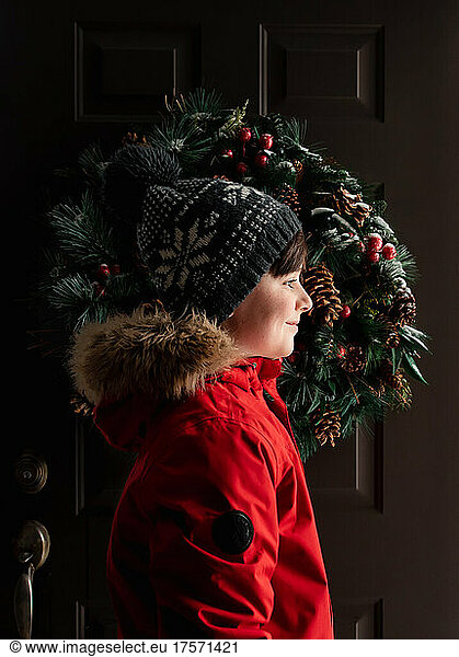 Happy boy in red coat and winter hat standing in doorway in winter.