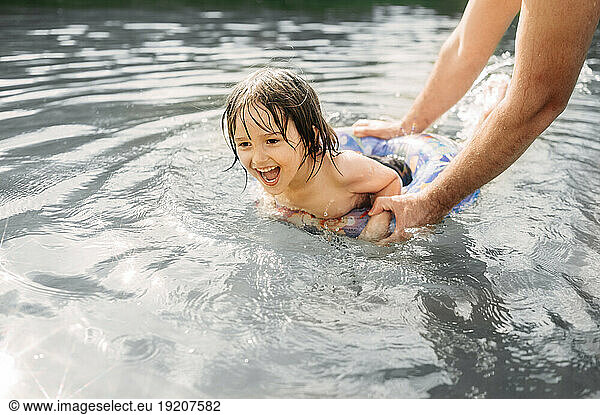 Happy boy learning swimming with father in river inflatable swim ring