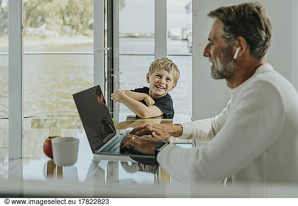Happy boy looking at father working on laptop